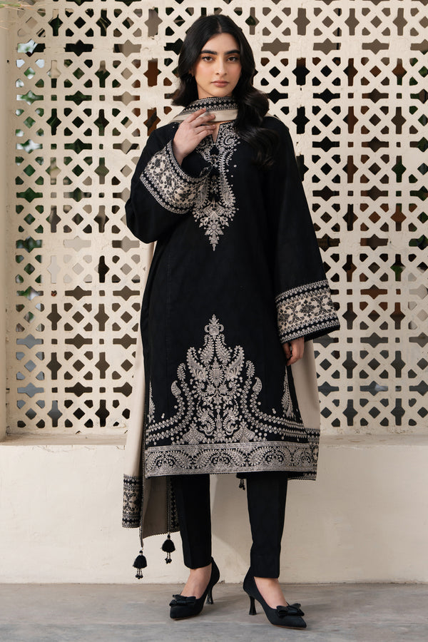 Woman wearing a black embroidered outfit in front of a decorative wall.